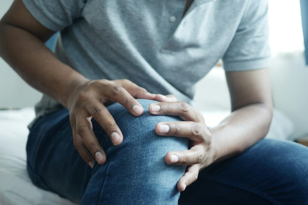 Nahaufnahme ein Mann in sitzender Position hält sich mit beiden Händen sein schmerzendes Knie